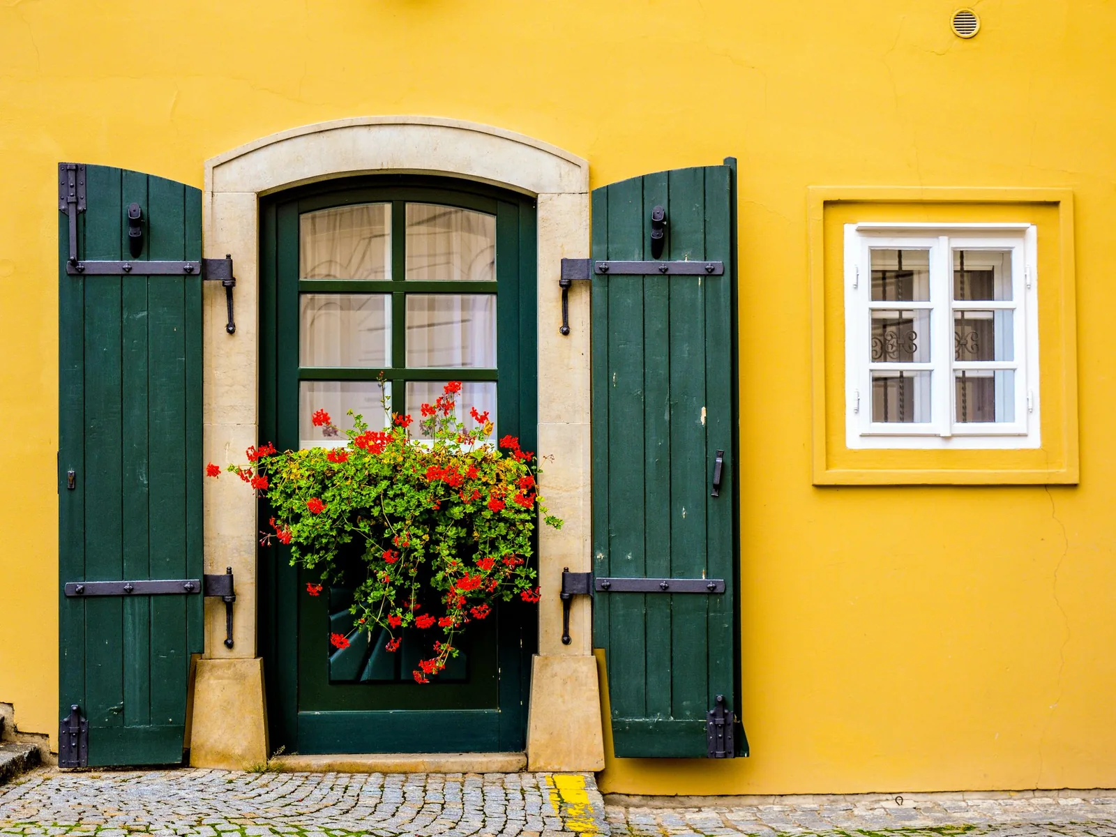 Yellow painted house wall with green shutters and front door