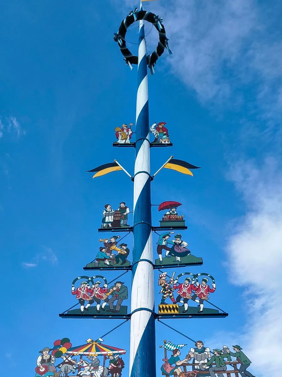 Weiß-blauer Maibaum mit bemalten Zunftfiguren vor blauem Himmel