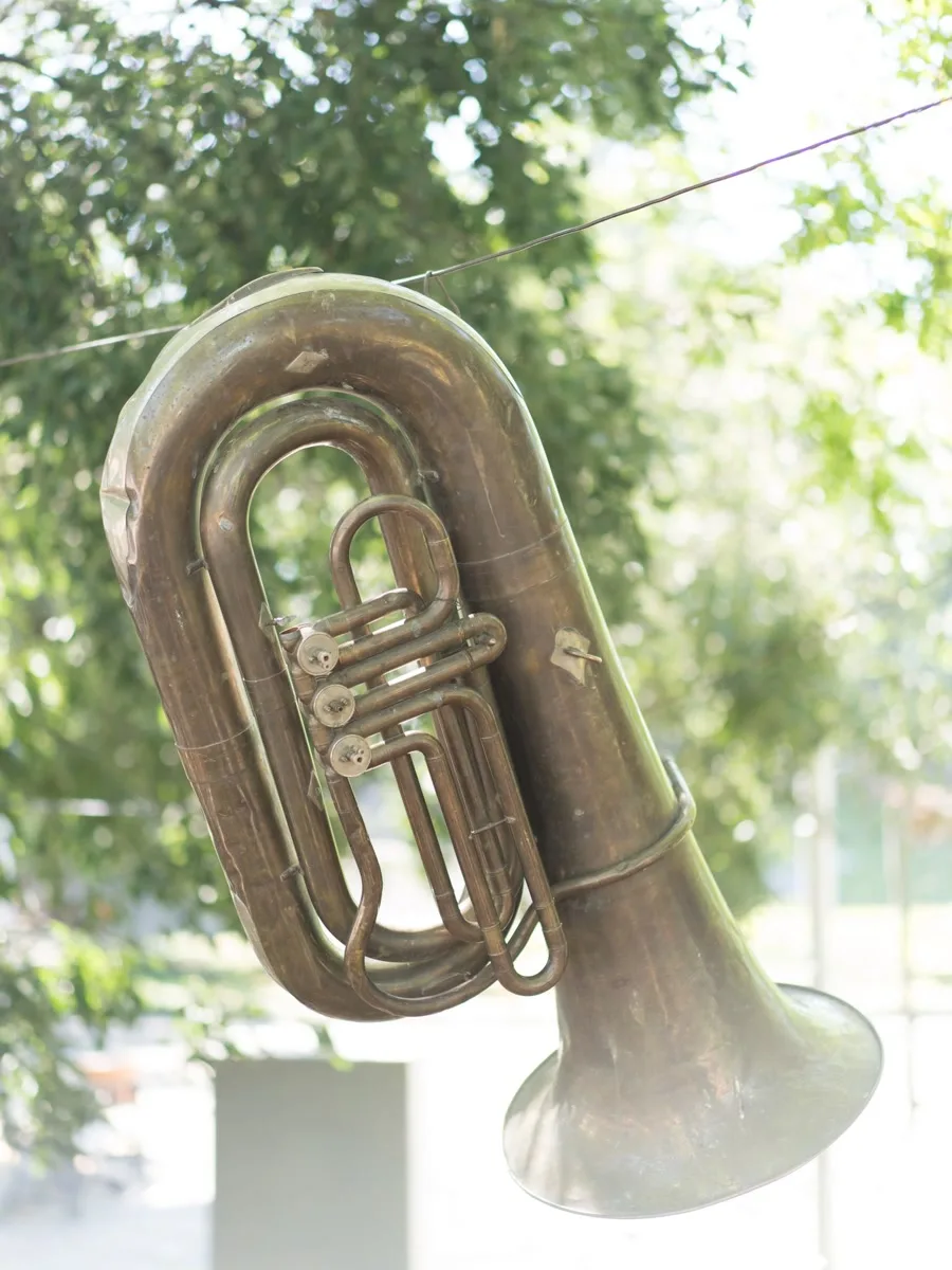 Alte Tuba aus Messing hängt an einem Draht unter Bäumen